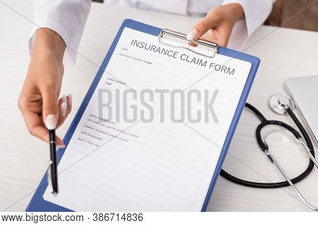 Partial View Of Doctor Holding Insurance Claim Form On Clipboard Near Stethoscope On Desk