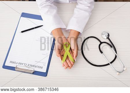 Top View Of Psychologist Holding Green Awareness Ribbon Near Insurance Claim Form And Stethoscope, M
