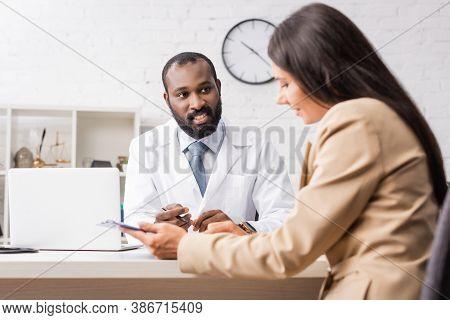 Brunette Woman Holding Clipboard With Diagnosis Near African American Doctor