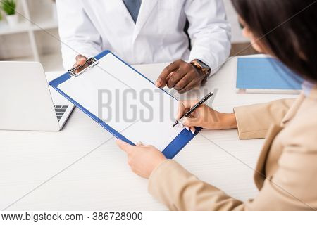 Cropped View Of Woman Holding Pen And Clipboard With White Paper Near African American Doctor