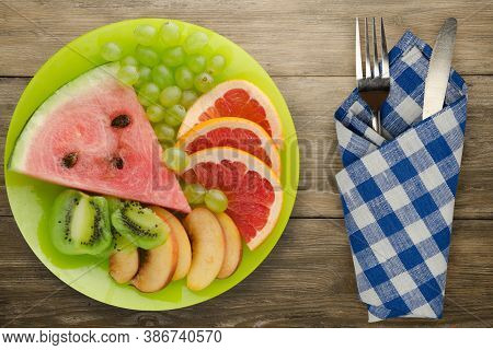 Sliced Fruit On A Borwn Wooden Background. Sliced Fruit On A Light Green Plate Fork And Knife Top Vi