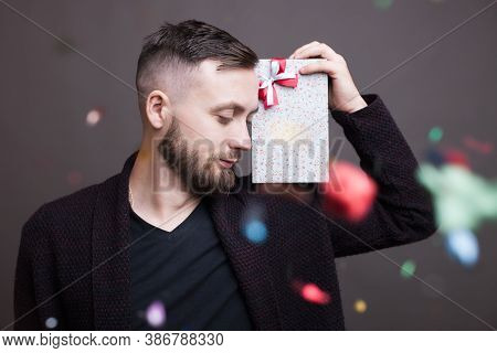 Bearded Caucasian Man With A Present On His Shoulder Is Posing In Formal Wear On A Gray Studio Wall 