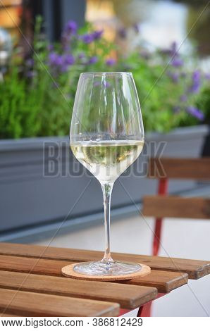 Close Up Of Glass Of White Wine Standing On A Wooden Table, Flower Pot In Background