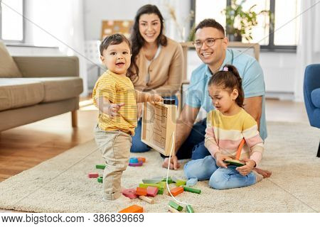 family and people concept - happy mother, father, little daughter and baby son playing with wooden toys at home