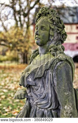 Side Detail Of Old  Green Moss Covered Statue Of The Girl With Flowers In Autumn