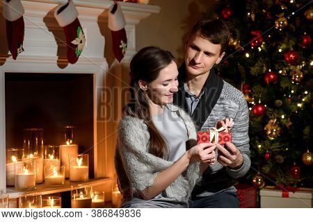 Family Couple Surprising Each Other With Christmas Presents. Husband Closing Eyes Of His Excited Wif