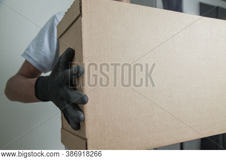 Detail Of Man With Black Gloves Holding A Cardboard Box For Delivering Products On Gray Background. 