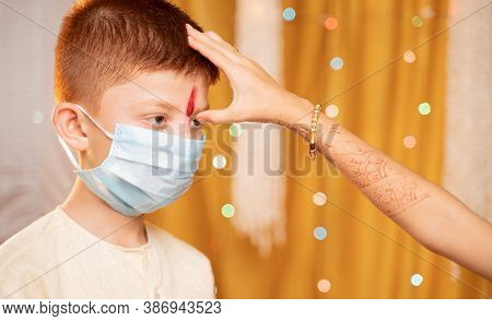 Close Up Hands Of Sister Applying Tilaka Or Mark To Forehead Of Brother With Medical Mask During Bha
