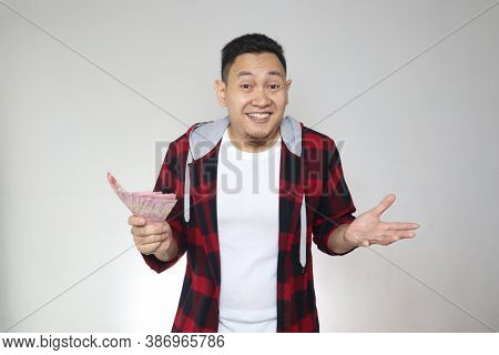 Portrait Of Happy Young Indonesian Man Holding Rupiah Money, Smiling Laughing Winning Gesture, Over 