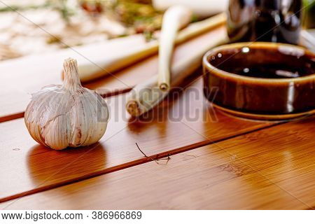 The Garlic Head And Lemongrass Stalks Lie On A Wooden Table
