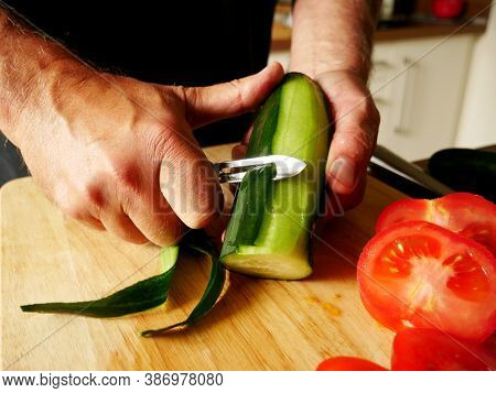 Man Peeling A Cucumber On A Wooden Board.