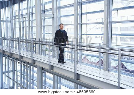 Longitud total del empresario envejecido medio caminando por la barandilla en la oficina moderna