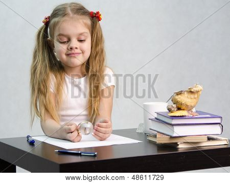 The girl thoughtfully and effortlessly turns the glass globe, sitting at the table in the image