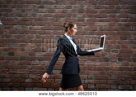 Billede af selvsikker forretningskvinde med laptop gåture langs mur