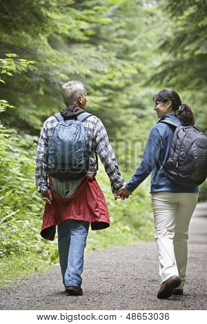 Full length rear view of a couple walking on forest road amid lush trees