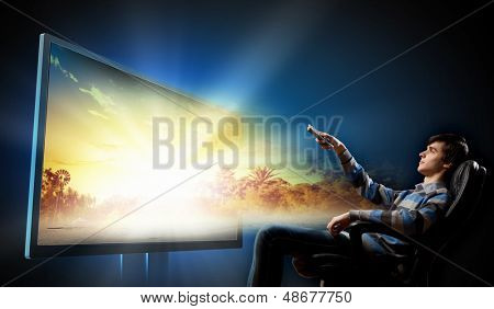 Giovane uomo in poltrona con fare clic su guardare la TV