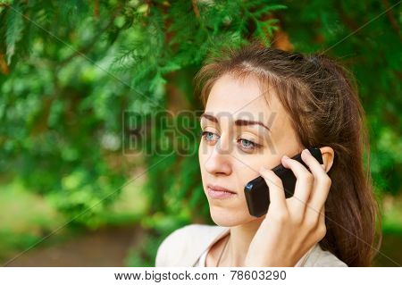 Girl Talking On The Phone On A Background Of Green Trees