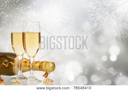 Glasses with champagne and bottle over fireworks and sparkling holiday background