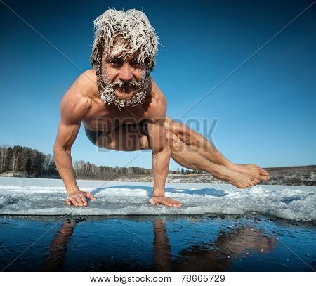 Man with frozen hair doing yoga exercise (parsva bakasana) on the ice