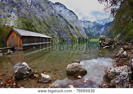 Cloudy day at Lake Koenigssee. Boathouse connected to the coast wooden decking. Clouds and mountains reflected in the water