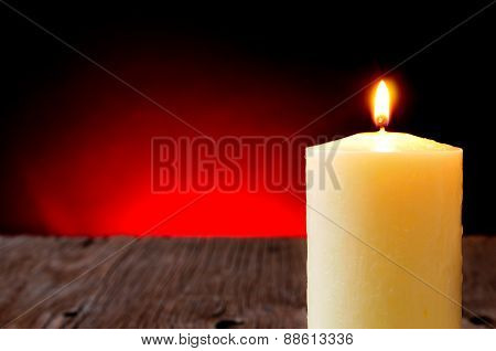 closeup of a lit candle on a wooden rustic table and a red lighted background