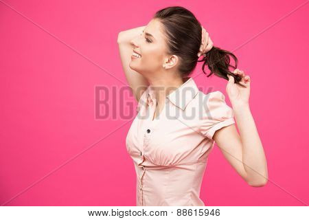 Side view portrait of a smiling woman holding her hair over pink background