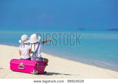 Little adorable girls with big suitcase on tropical white beach during summer vacation