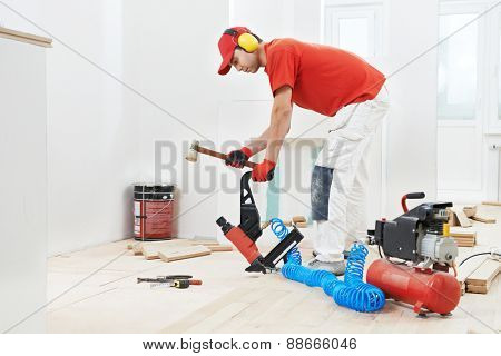carpenter worker installing wood floor parquet board during flooring work with hammer