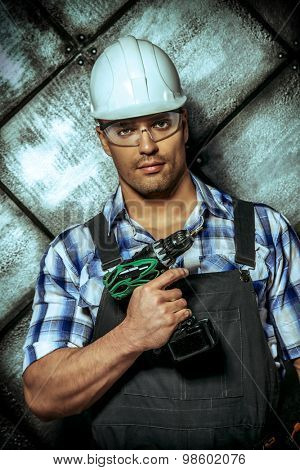 Close-up portrait of a handsome costruction worker standing in uniform and helmet over grunge industrial background. Job, occupation. 