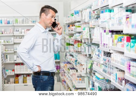 Confused mid adult man using mobile phone while looking at products in pharmacy