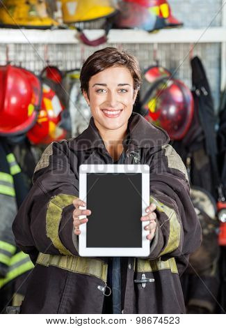 Portrait of happy firewoman showing digital tablet at fire station