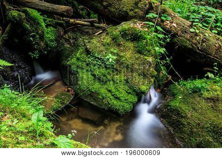 a small river in the German black forest between rocks with moss on top