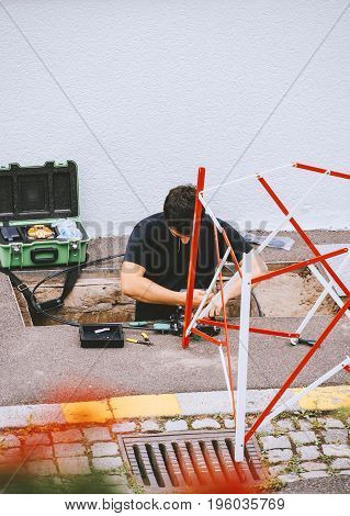 PARIS FRANCE - JUL 12 2017: Young worker inside sewage manhole hole - telecommunication internet provider company working on implementation of fiber optic cables in sewage system using fiber optic welding machine to cover the whole Paris area