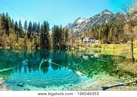 Traditional hotel at waterside of clear alpine lake. Snow covered mountains and blue sky.