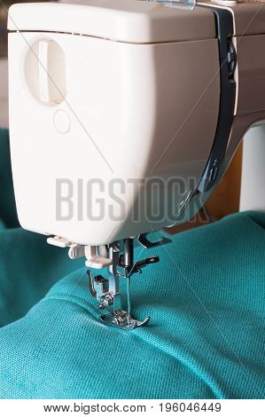 Close up of sewing machine working with turquoise fabric