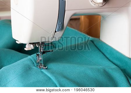 Close up of sewing machine working with turquoise fabric