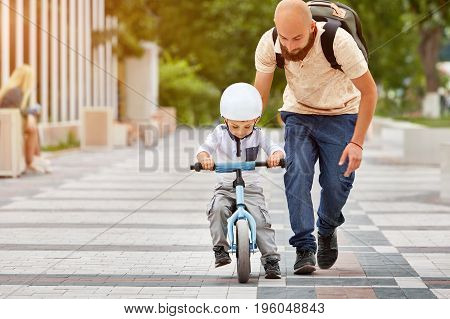 Father help his son ride a bicycle in city park