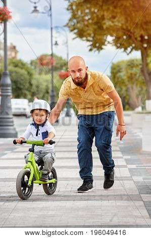 Father help his son ride a bicycle in city park