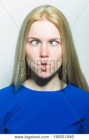Woman squinting eyes on funny face. Young woman with crossed grey eyes healthy skin and long blond hair in blue dress isolated on white. Grimace and facial expression. Strabismus