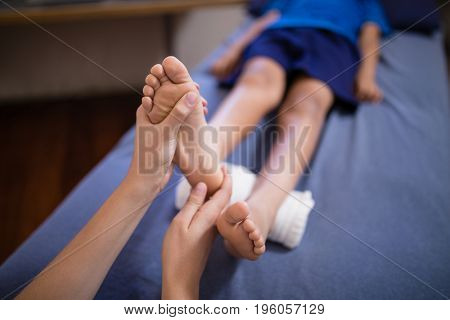 High angle view of boy lying on bed receiving foot massage from female therapist at hospital ward