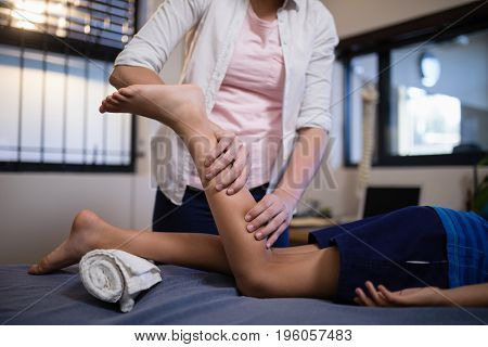 Low section of boy lying on bed while receiving calf massage from female therapist at hospital ward