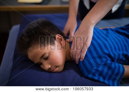 High angle view of boy sleeping on bed while receiving back massage from female therapist at hospital ward
