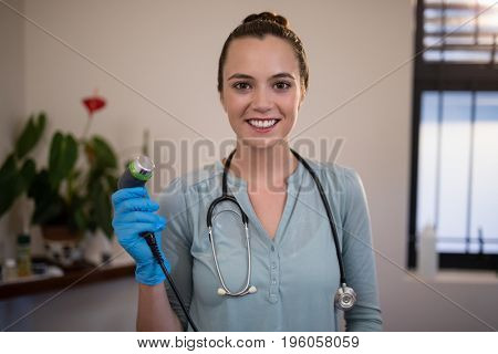 Portrait of smiling young female therapist holding ultrasound machine at hospital ward