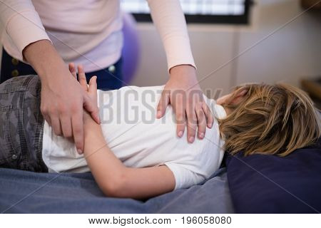 Female therapist examining arm of boy lying on bed at hospital ward