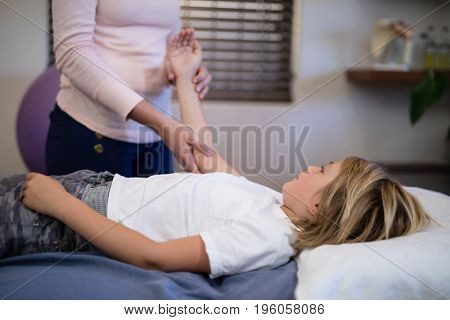 Midsection of female therapist examining arm with boy lying on bed at hospital ward