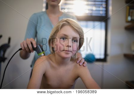 Blond boy sitting while female therapist using ultrasound machine at hospital ward