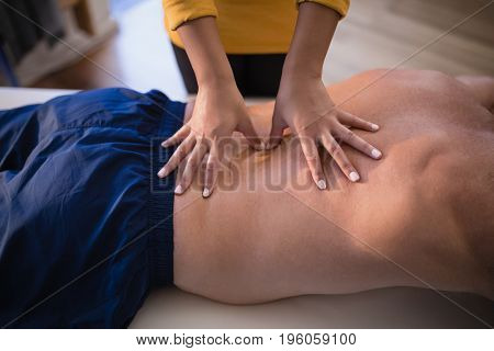 Midsection of female therapist giving back massage to shirtless male patient at hospital ward