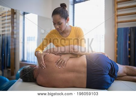 Female therapist massaging back of senior male patient at hospital ward