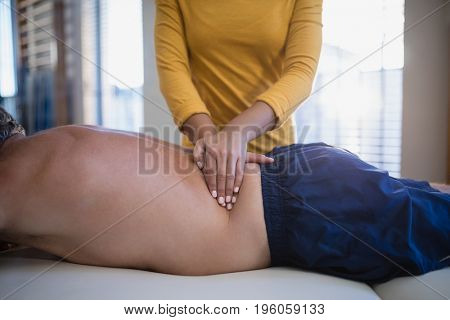 Midsection of female therapist giving back massage to shirtless male patient lying on bed at hospital ward