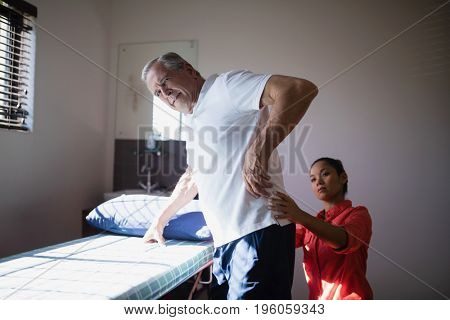 Senior man receiving back massage from female therapist at hospital ward
